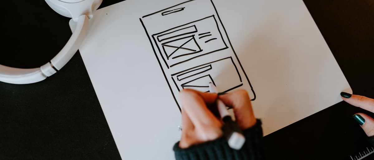 Designer sketching interface wireframes on paper beside headphones