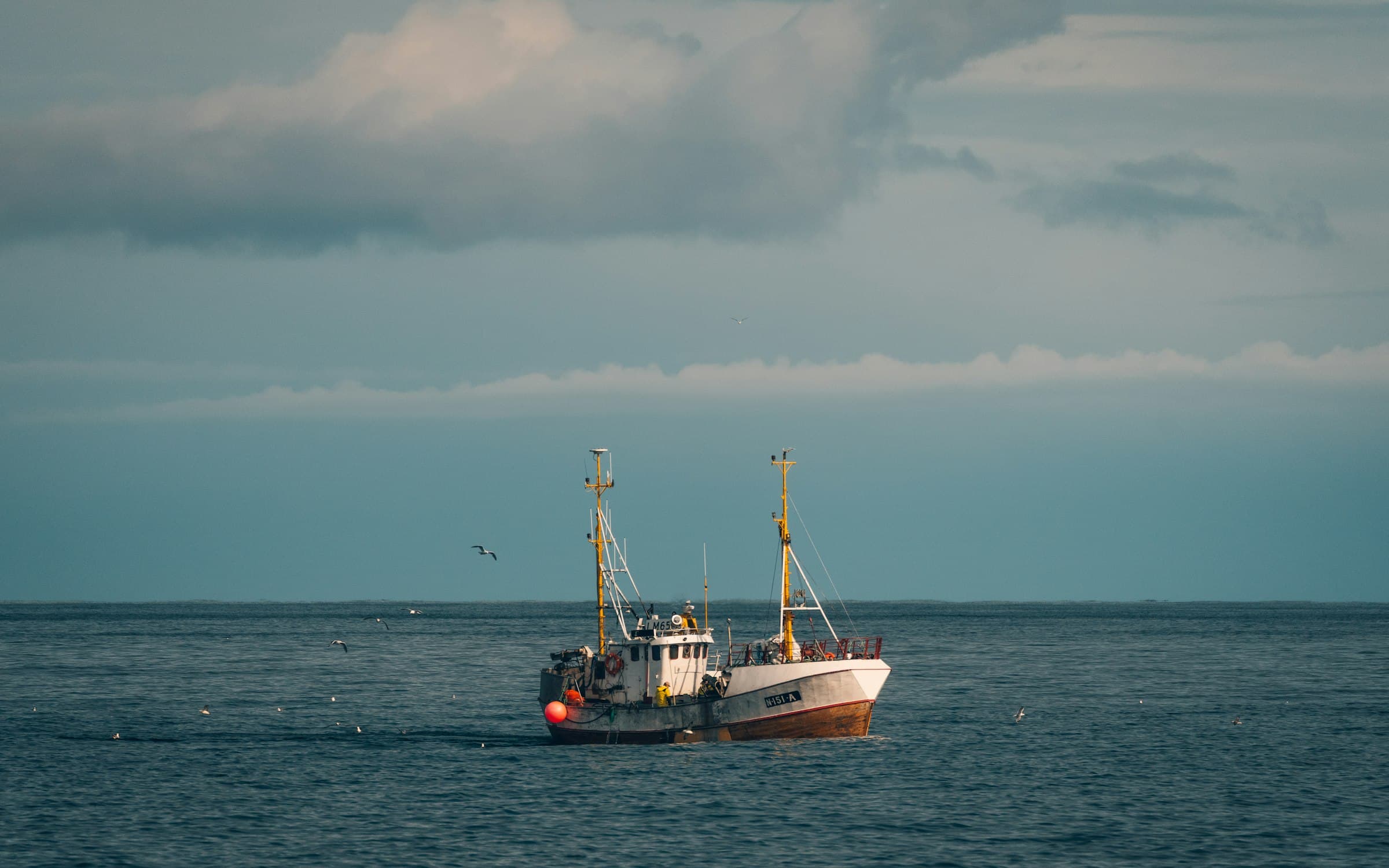 A small working boat crossing flat grey water beneath a low coastal sky